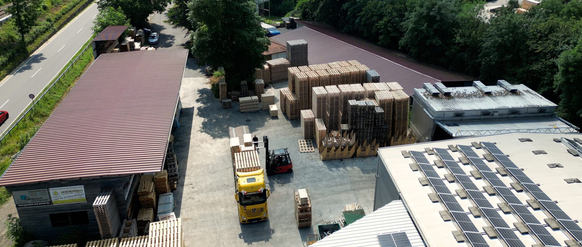 Übersichtliche Luftaufnahme eines Lagers mit Trucks und Paletten auf dem Gelände.